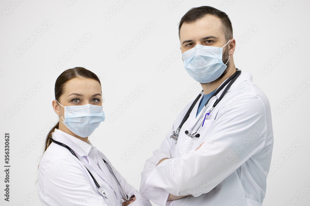 Two male and female doctors in white lab coat and protective masks standing opposite each other and looks at camera on white background. Healthcare support, medical workers, pandemic virus infection Two male and female doctors in white lab coat and protective masks standing opposite each other and looks at camera on white background. Healthcare support, medical workers, pandemic virus infection