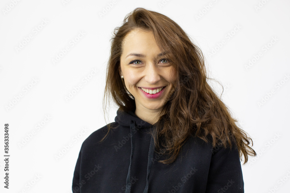 Portrait of young beautiful smiling girl with long dark curly hair wearing trendy hipster black hoodie looking at camera isolated on white background. Happy positive woman, human emotions Portrait of young beautiful smiling girl with long dark curly hair wearing trendy hipster black hoodie looking at camera isolated on white background. Happy positive woman, human emotions