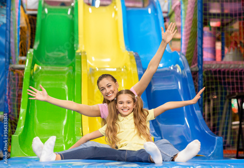 Valokuva Smiling mother and her daughter riding slide together at indoor kids playground