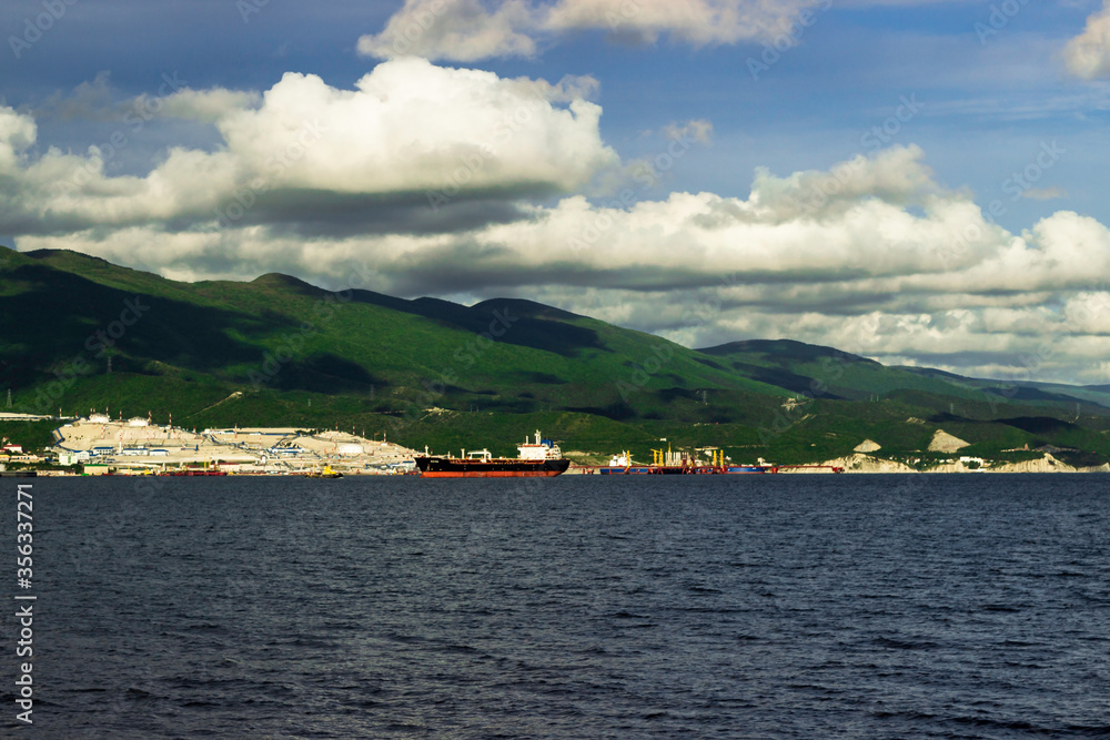 View at cloudy sky over the mountains and sea ship on the raid near the port in bay near Novorossiysk at sunny day.