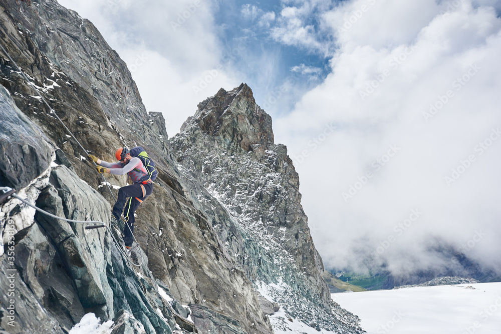 Rock climber in safety helmet using fixed rope while ascending rocky