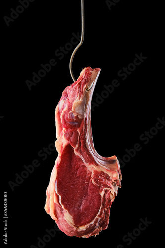Beef ribeye steak bone-in on steel hook on black background