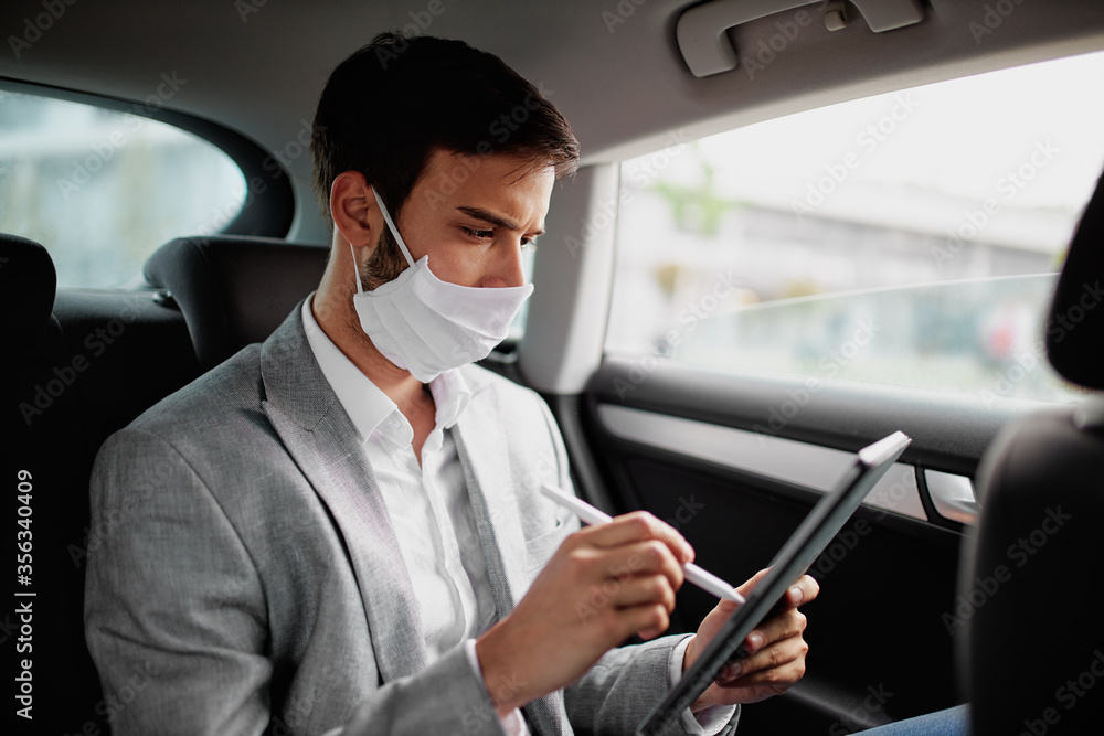 Young man wearing a face mask sitting in the car and using digital tablet