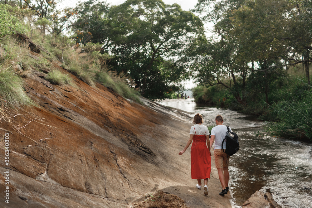 Couple admires a beautiful waterfall. Couple in love at the waterfall. Boy and girl at the falls. A guy and a girl traveling. The couple travels around Asia. Waterfalls in Sri Lanka. Honeymoon trip
