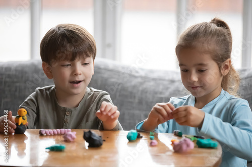 Little preschooler boy and girl children engaged in creative activity with playdough at home, small brother and sister play with modeling clay Play-Doh, do figures together, craft, hobby concept photo