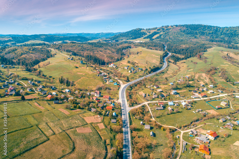 Panoramic aerial view of the mountain highway and village in spring. Beautiful skyview countryside landscape. Carpathian mountains. Ukraine