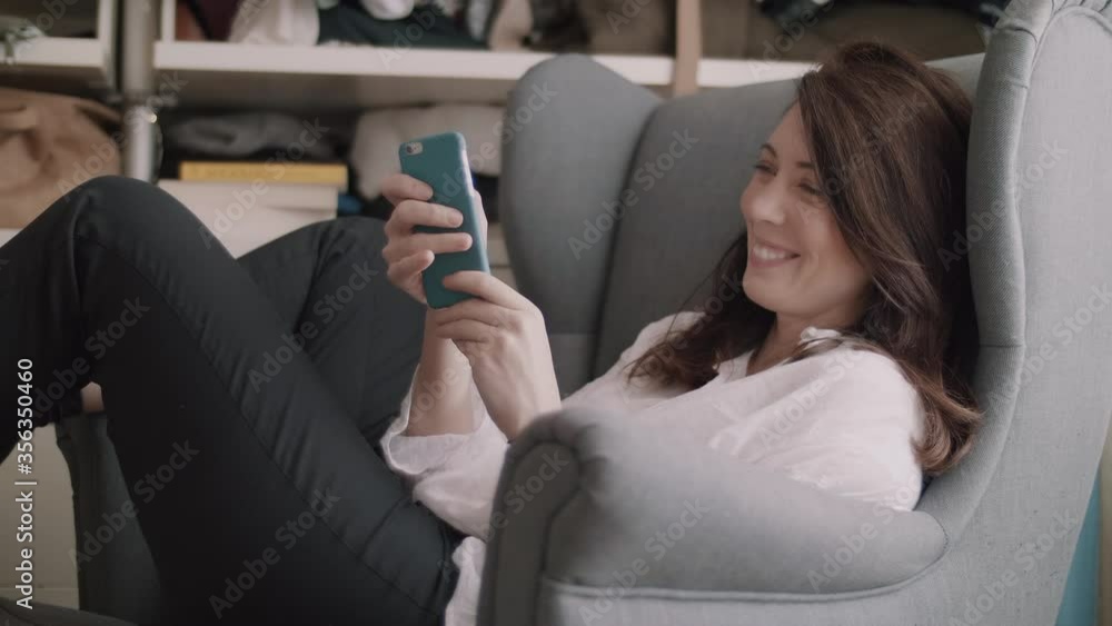 Brunette woman smiling and chatting via phone while sitting on a comfy sofa chair Brunette woman smiling and chatting via phone while sitting on a comfy sofa chair
