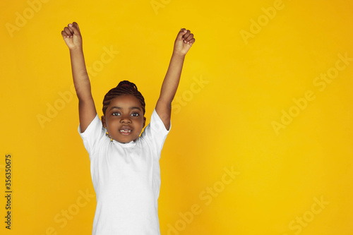 Strong, winner, leader. Little african-american girl's portrait on yellow studio background. Cheerful, beautiful kid. Concept of human emotions, expression, sales, ad. Copyspace. Looks cute.