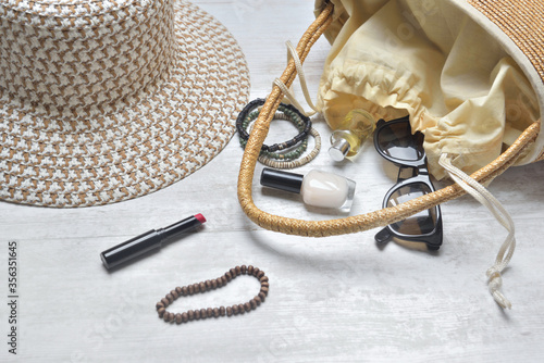 hand bag and hat with female accessories spilled on white table