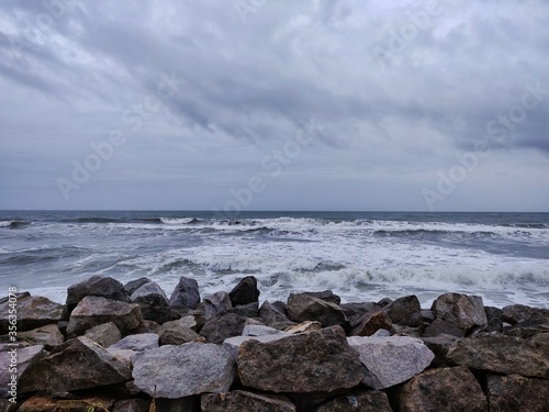 A picture of beach with rocks on the shore and cloudy sky on background. The sea is violent with strong waves in this picture. Kappil Beach (Varkala Town), Kerala. photo