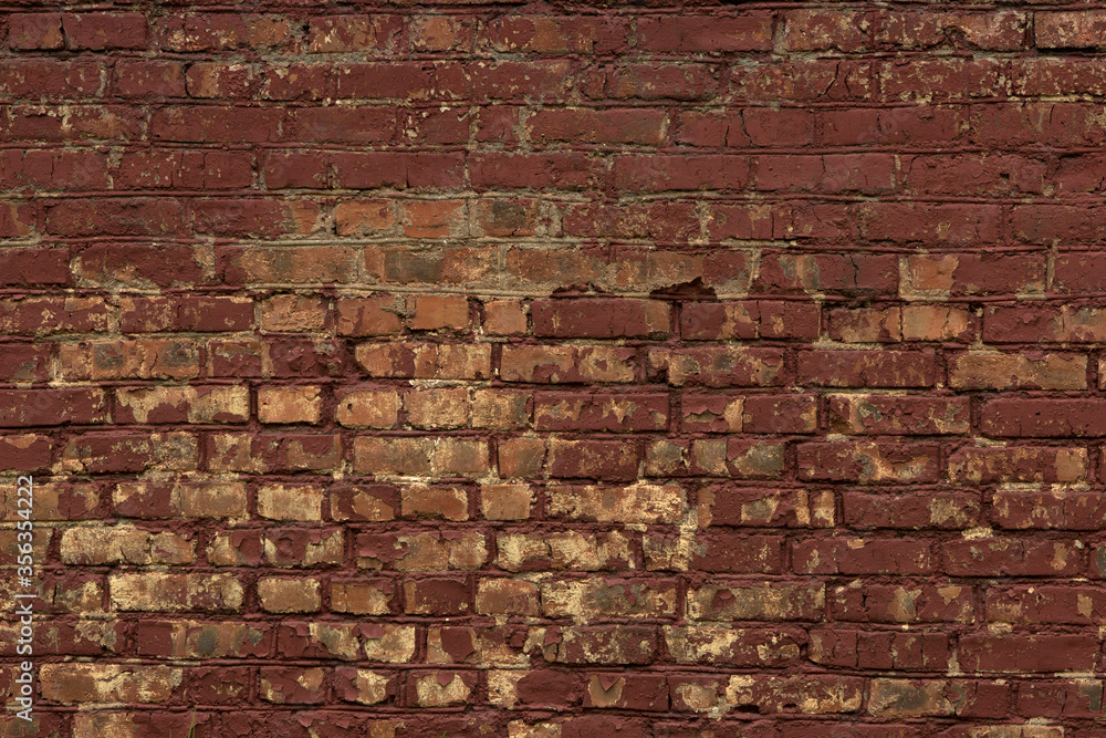 Obraz premium Red curved old brick wall with uneven masonry, stained with paint, painted burgundy and cracked