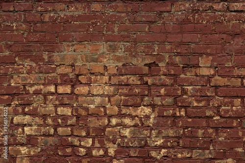 Red curved old brick wall with uneven masonry, stained with paint, painted burgundy and cracked