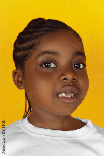 Looking on camera attented, close up. Little african-american girl's portrait on yellow studio background. Cheerful kid. Concept of human emotions, expression, sales, ad. Copyspace. Looks cute. © master1305