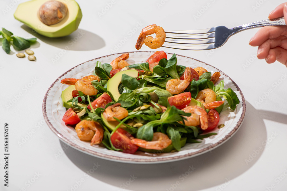 partial view of woman eating fresh green salad with cherry tomatoes, shrimps and avocado on white background partial view of woman eating fresh green salad with cherry tomatoes, shrimps and avocado on white background