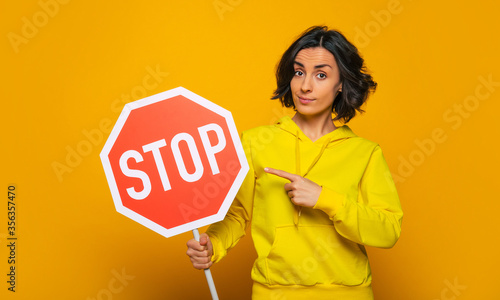 Persistent requirement. Half-length photo of confident and persistent young girl, dressed in a yellow hoodie, earnestly pointing on 