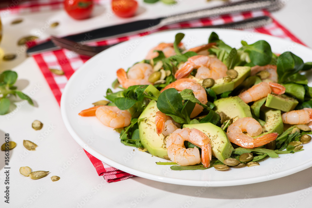 fresh green salad with shrimps and avocado on plate and plaid napkin on white background fresh green salad with shrimps and avocado on plate and plaid napkin on white background