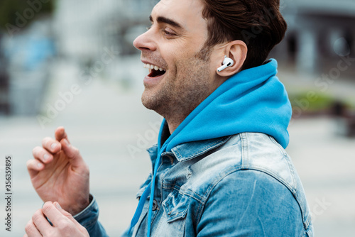 Side view of happy man listening music in earphones on urban street