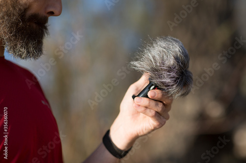 Obraz na płótnie Bearded man holding microphone with a wind noise protection zoom