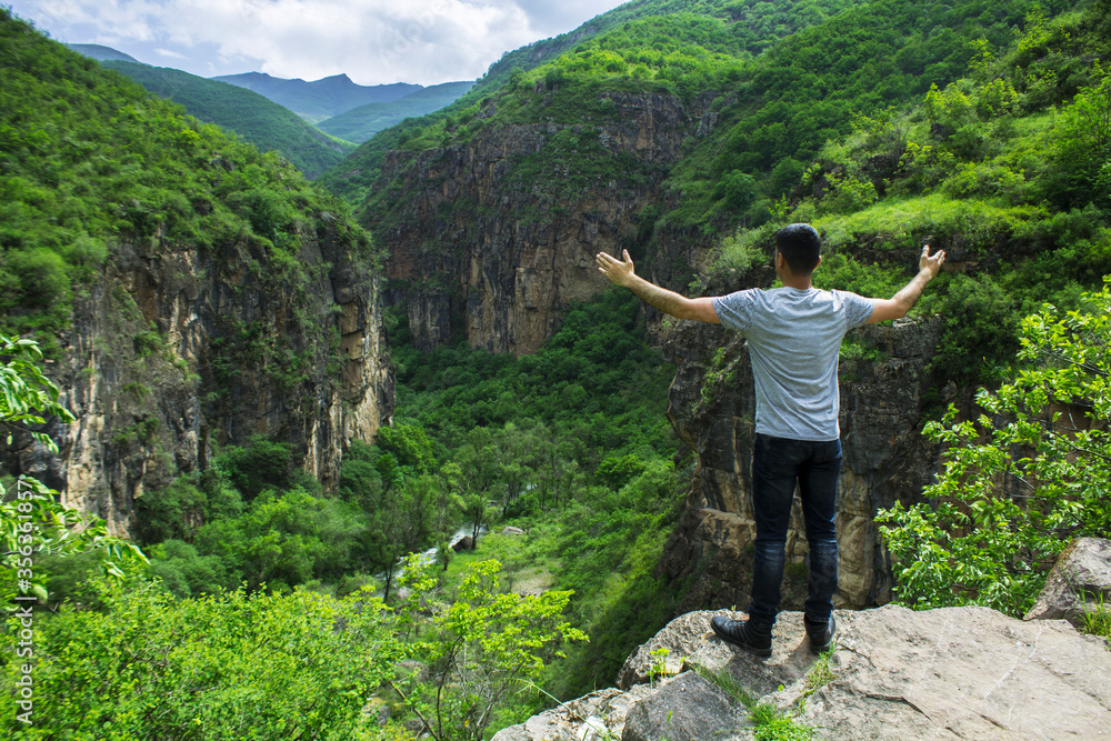 A man with open hands stands by a cliff