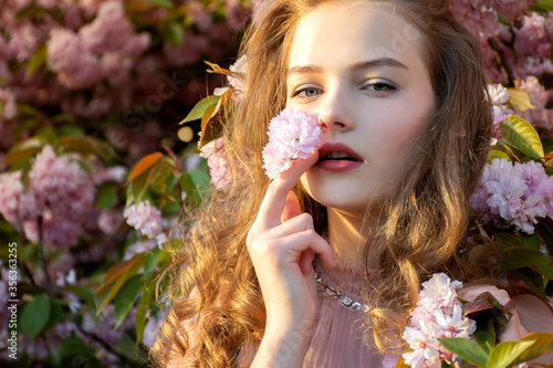 Closeup portrait of teenage girl in delicate sakura flowers. Look into the camera.