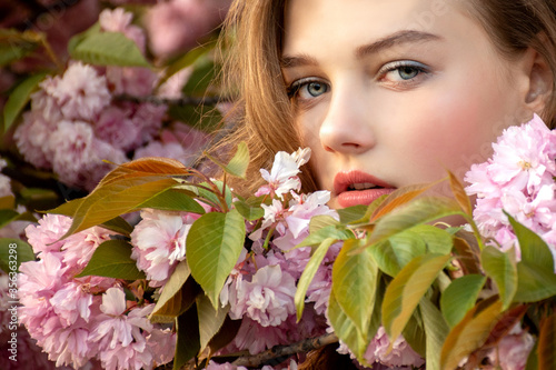 Closeup portrait of teenage girl in delicate sakura flowers. Look into the camera.