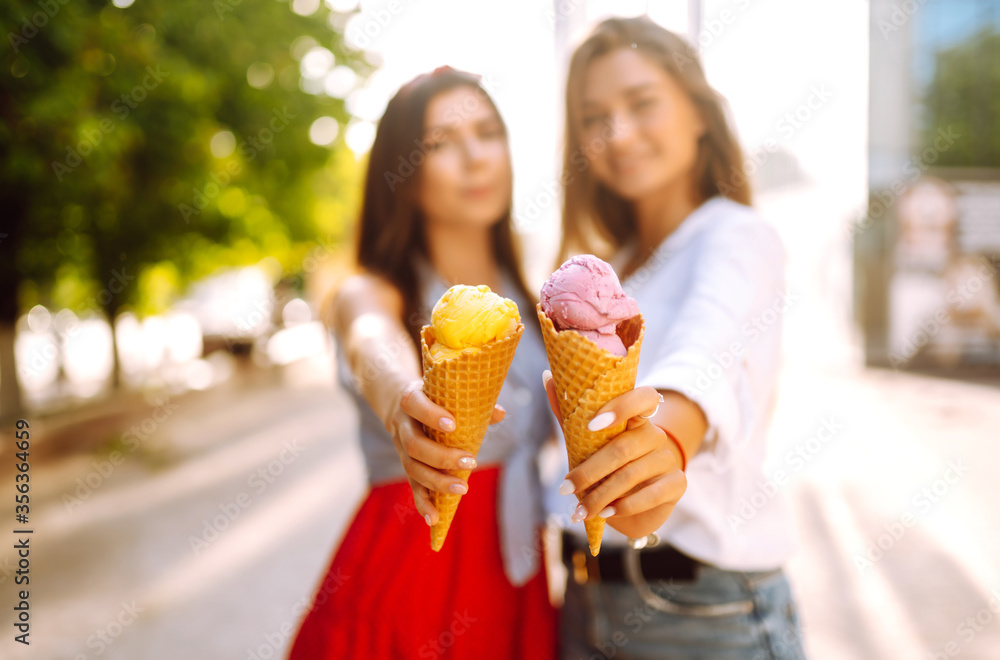 Ice cream in the hands of beautiful young girls. Two female friends eat ice cream while walking in the park. Summer and vacation concept.