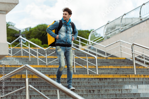 Selective focus of smiling courier with thermo backpack walking down on stairs with railing © LIGHTFIELD STUDIOS