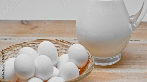 Eggs in basket and jug of milk on wooden surface isolated on grey photo