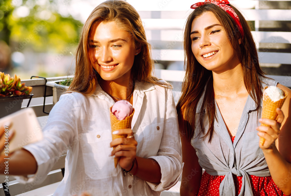 Two young girl friends makes selfie with ice cream. Looking at camera and smiling. Summer and vacation concept. Two young girl friends makes selfie with ice cream. Looking at camera and smiling. Summer and vacation concept.