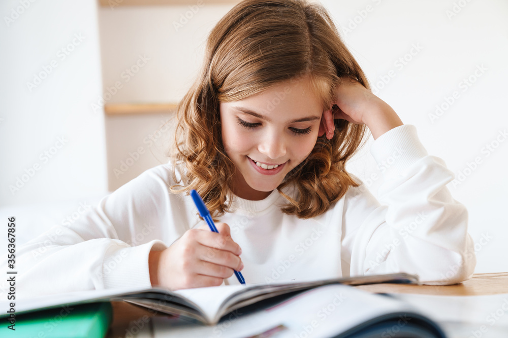 Photo of happy girl writing in exercise book while doing homework Photo of happy girl writing in exercise book while doing homework