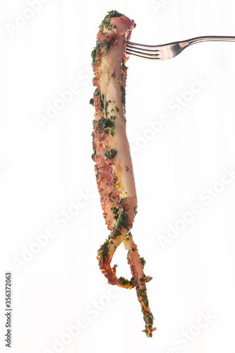 Two seasoned and cooked octopus tentacles hanging from a fork. Vertical. White background and copy space.