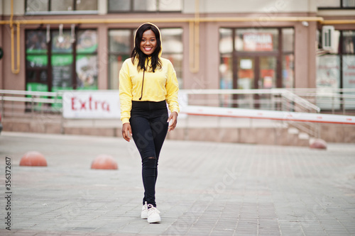 Hipster african american girl wearing yellow hoodie posing at street.