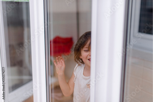 Niña alegre mira a través del cristal de una ventana