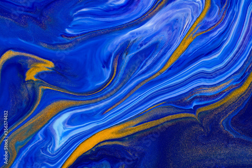Fluid art texture. Abstract backdrop with swirling paint effect. Liquid acrylic picture with chaotic mixed paints. Classic blue color of the year 2020. Blue, golden and white overflowing colors