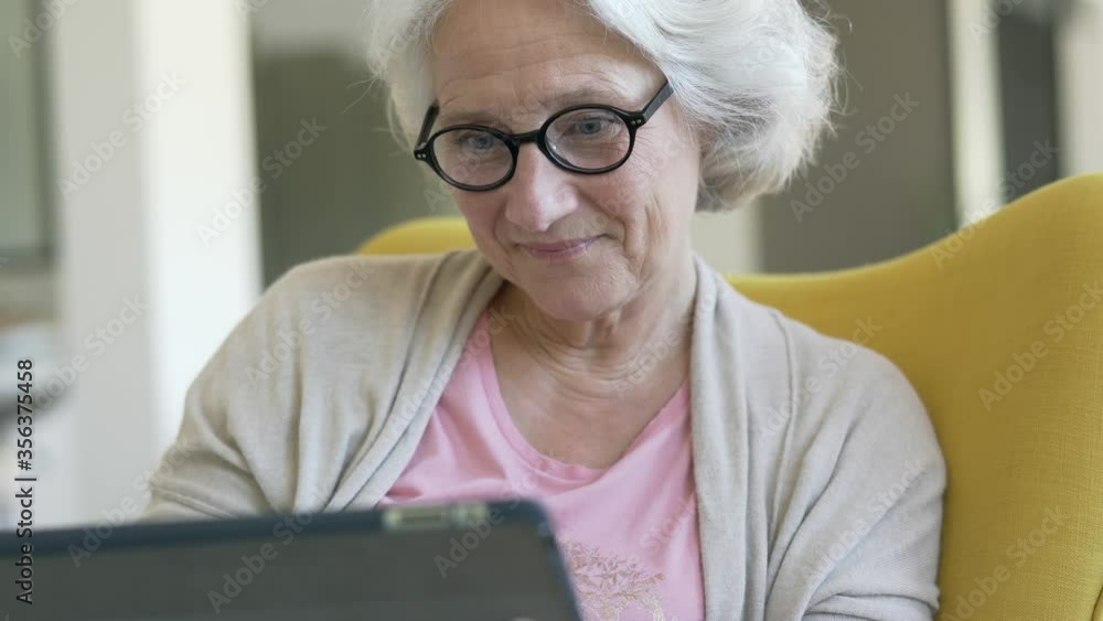 Senior woman relaxing in armchair and using digital tablet Senior woman relaxing in armchair and using digital tablet