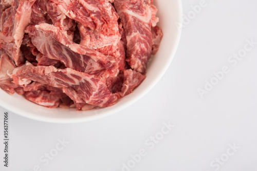 close up copy space shot of sliced raw beef fillet pieces in a white bowl on a white background