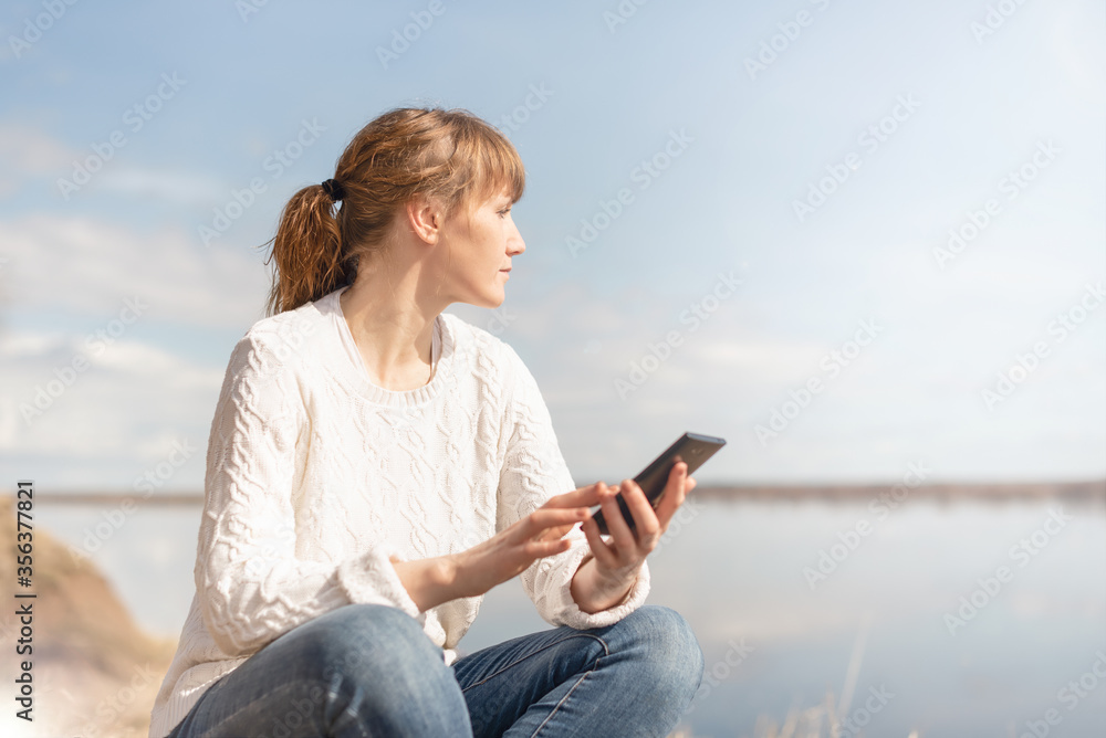 woman with calm look sitting looking at phone outdoors