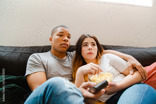 Interracial couple sitting on the sofa watching a movie and eating popcorn photo