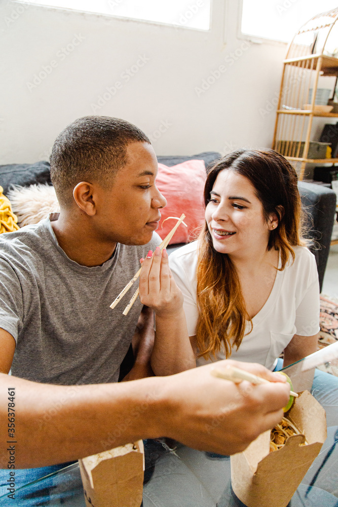 Fototapeta premium Interracial couple in love eating takeaway chinese food at home