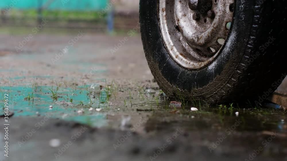 during the rain, an old, dirty wheel stands among puddles. Raindrops dripping during the rain, an old, dirty wheel stands among puddles. Raindrops dripping
