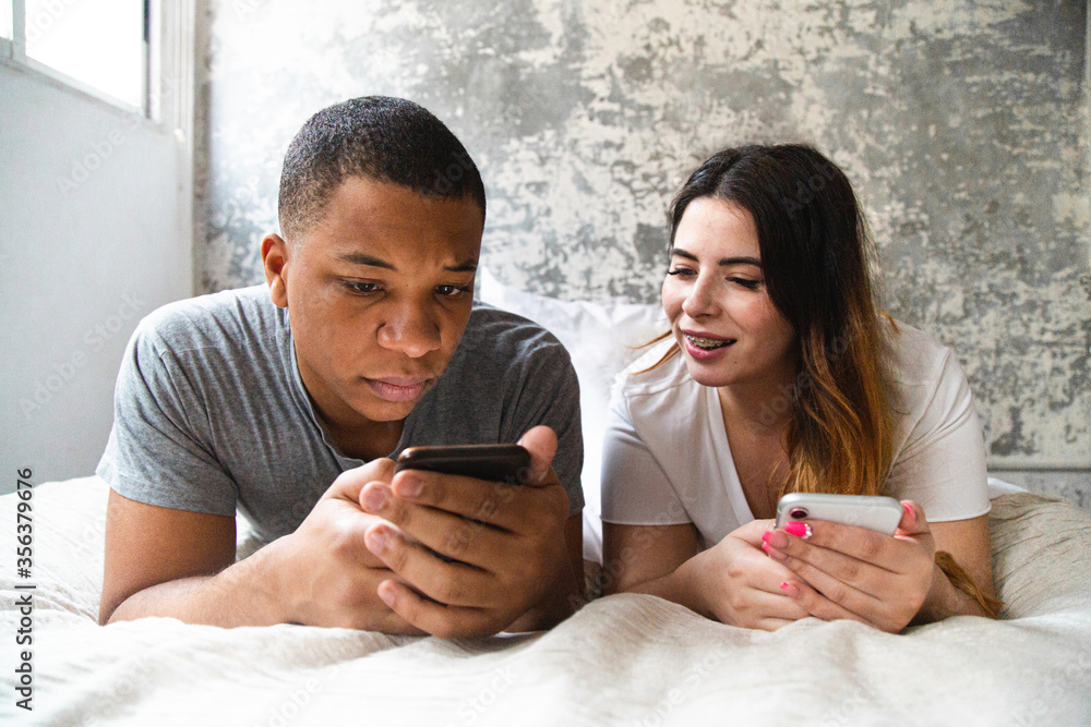 Interracial couple lying on the bed and looking at their phones Interracial couple lying on the bed and looking at their phones