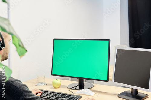 Man at his workplace with a computer and a green screen