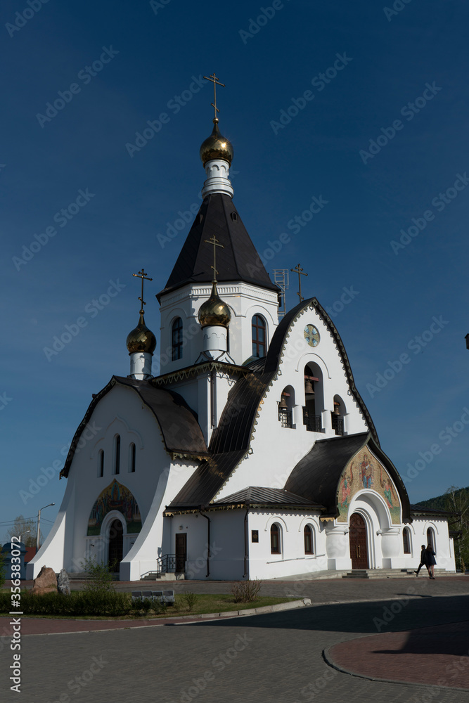 White Church on a background of blue sky. Church with a bronze roof and golden domes.