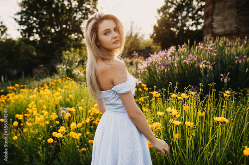 Young slim woman with long blonde hair in the field of yellow flowers in golden hour.