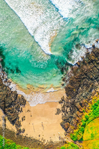 Top down aerial view of a beach with waves, rocks and sand.