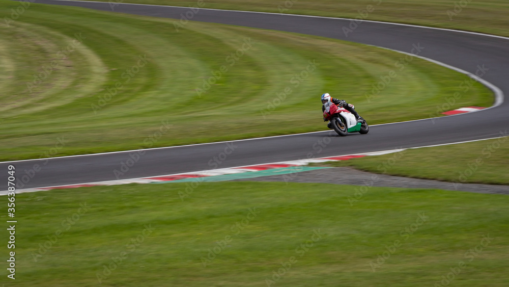 A panning shot of a red, white and green racing bike cornering on a track