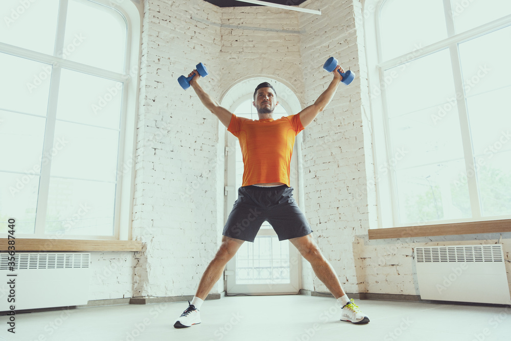 Dumbbell. Young caucasian man training at home during quarantine of coronavirus outbreak, doing exercises of fitness, aerobic. Staying sportive during insulation. Wellness, sport, movement concept. Dumbbell. Young caucasian man training at home during quarantine of coronavirus outbreak, doing exercises of fitness, aerobic. Staying sportive during insulation. Wellness, sport, movement concept.