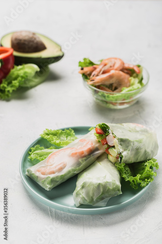 Spring rice paper roll with shrimp, avocado, paprika, lettuce and cottage cheese on a bright plate on a white background.