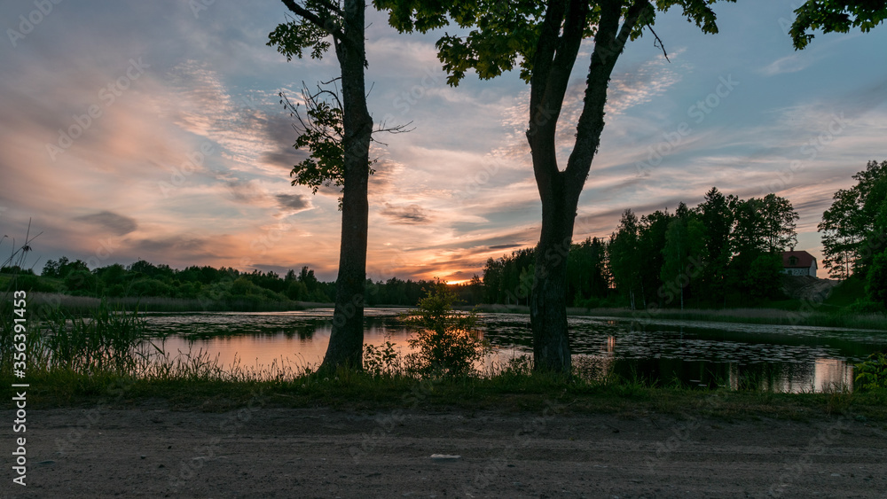 image with a beautiful colorful sunset over the lake, in the foreground the contours of trees and grass, Lielais Ansis, Rubene, Latvia