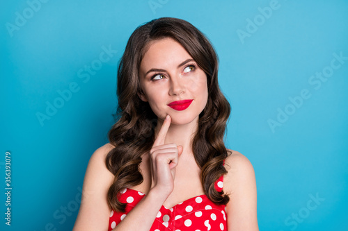Closeup photo of attractive curly lady minded good mood arms crossed look up empty space interested creative arm on chin wear red dotted dress singlet isolated blue color background